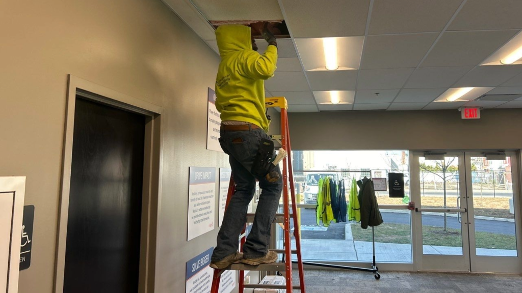 cabling tech on orange ladder installing cable in ceiling