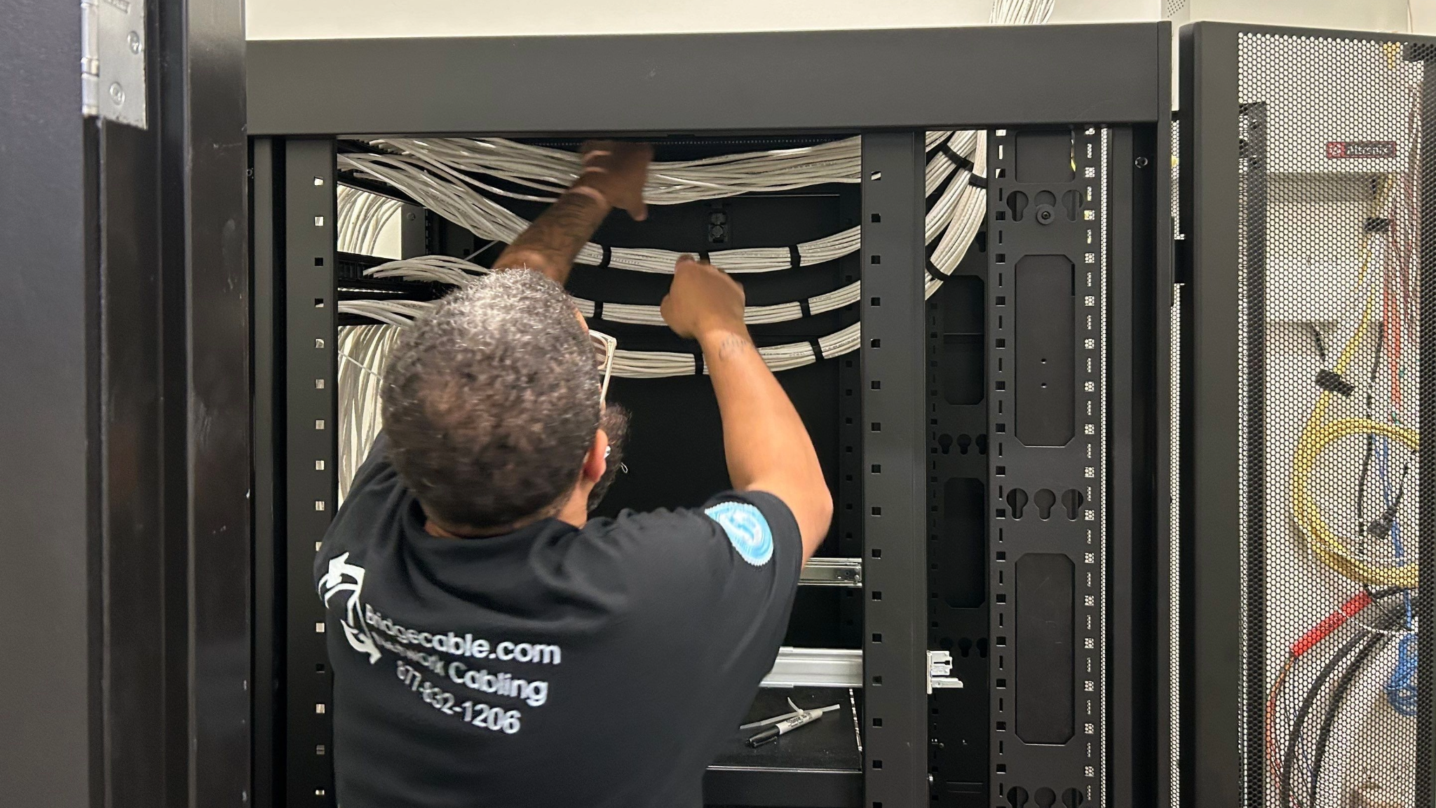 cabling tech in data rack putting black velcro ties on white cable