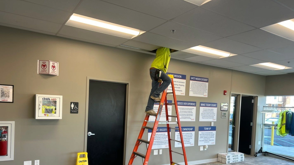 cabling tech on orange ladder in building doing cable install in ceiling