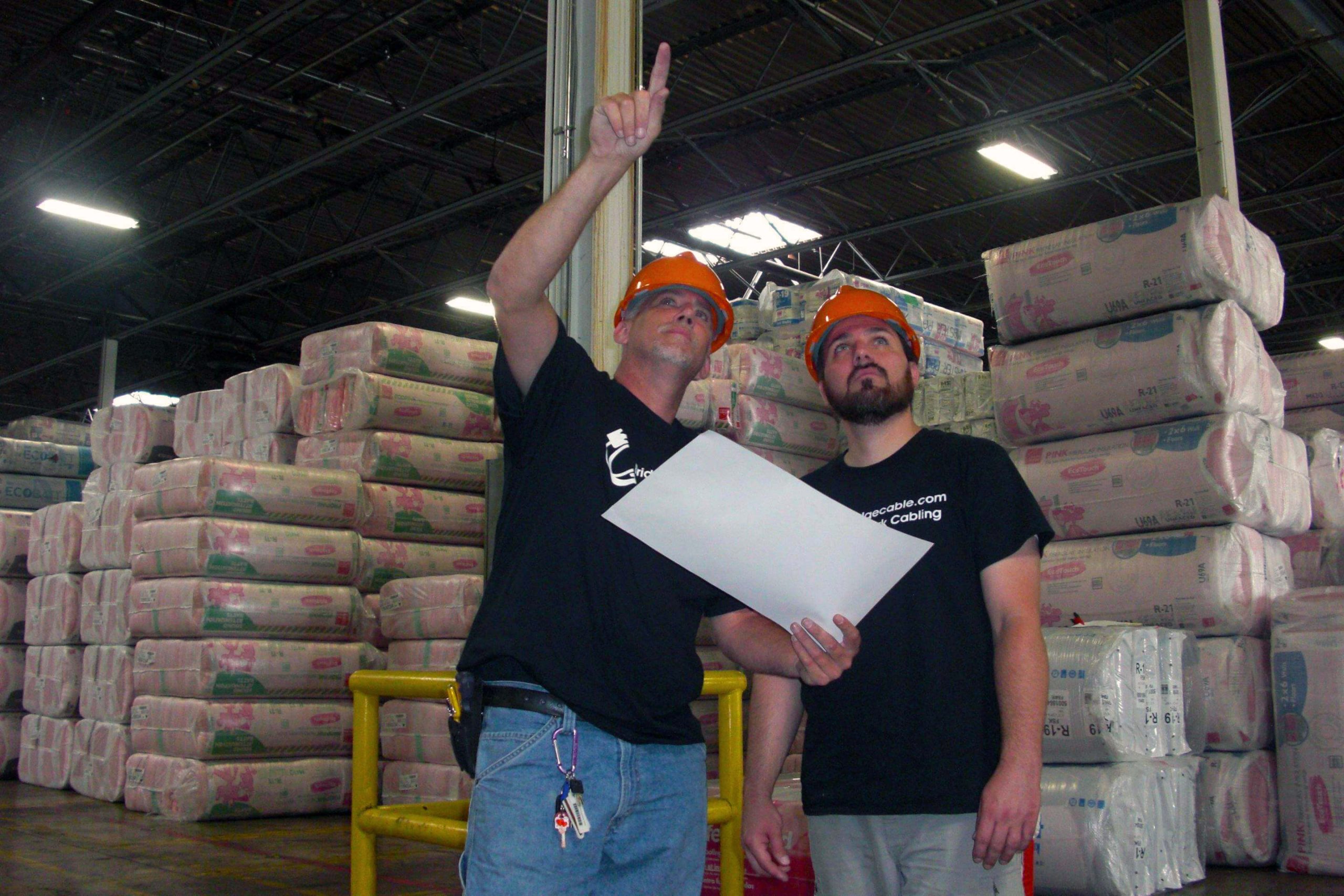 two cabling techs in warehouse looking at ceiling and reviewing site map