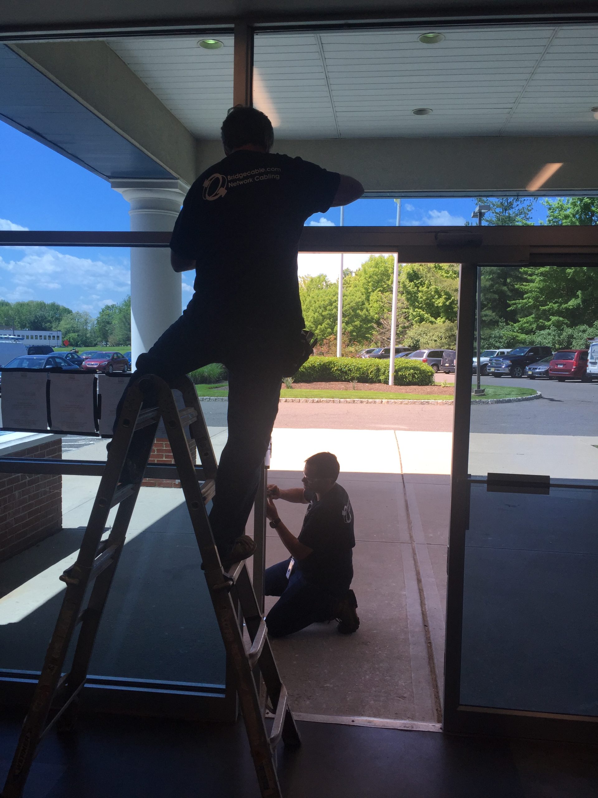 Two structured cabling technicians installing door access control on a main entrance.