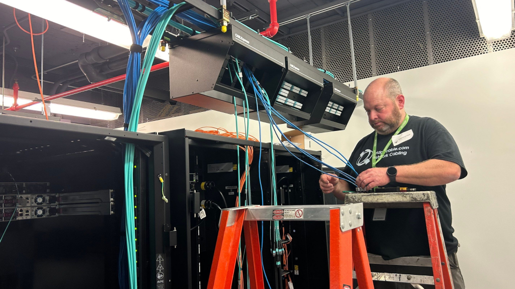 a tech in a black shirt doing cabling work on a ladder in a data center