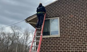 a tech in a black sweatshirt on a ladder working on security camera installs