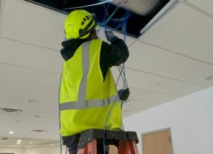network cabling tech in yellow vest on ladder