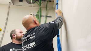 How to Read Genesis/Southwire Cable Part Numbers: A Complete Guide by Bridge Cable 4 Two Bridge Cable technicians installing and securing blue network cabling inside a commercial telecommunications room.