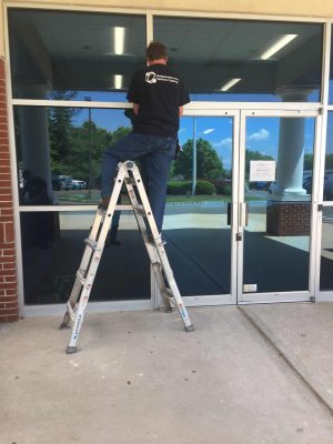 Retail Shrinkage Protection Solutions with Bridge Cable 3 Bridge Cable technician on ladder performing access control system installation above a commercial glass entry door.