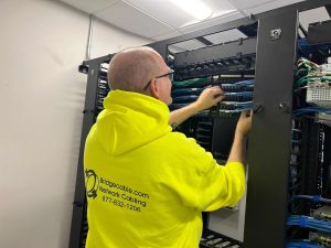 Retail Shrinkage Protection Solutions with Bridge Cable 2 Bridge Cable network cabling technician working on structured cabling and patch panel connections inside a server rack.