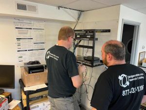 How Structured Cabling Supports Podcasters and Live Streamers 3 Bridge Cable technicians working on a wall-mounted network rack and structured cabling installation inside a commercial office.
