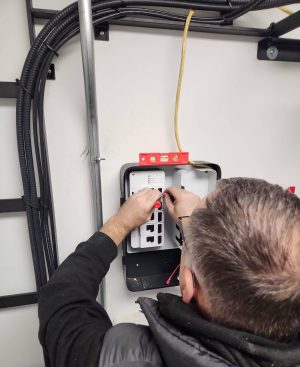 NAICS Code 238210 and Bridge Cable: Delivering Reliable Connectivity 4 Technician wiring and configuring an access control panel mounted on a wall during a commercial security system installation.