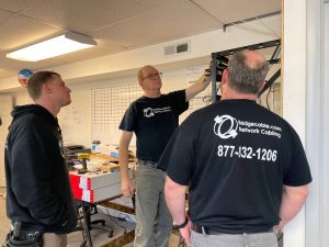 Why CommScope Certification Matters for Network Cabling 1 Three Bridge Cable network cabling technicians inspecting and installing cables in a wall-mounted network rack inside a commercial office environment.