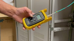 Mass Production Makes Single Mode Fiber More Affordable 2 Technician using a fiber optic power meter to test and certify a single mode fiber connection inside a network cabinet.