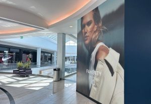 How ShopperTrak Solutions Improve Retail Performance 1 FAHERTY promotional wall graphic featuring a fashion model displayed in a shopping mall corridor near retail storefronts.