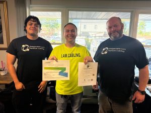 Getting Into Low Voltage Careers Through Trade Schools 1 Three network cabling professionals posing indoors while displaying structured cabling certification certificates.