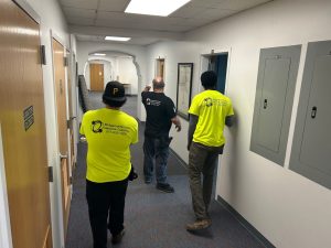 Discover Why Companies Upgrade Ethernet Cabling Harrisburg PA 2 Three technicians wearing Bridgecable Network Cabling branded shirts walking down an office hallway past electrical panels during a site walkthrough for ethernet cabling Harrisburg PA.