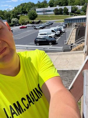 CCTV Contractor: CCTV vs AI Video Analytics in 2026 1 Technician in a neon yellow "I AM CABLING" shirt standing on a rooftop platform overlooking a commercial parking lot during a cabling installation project.