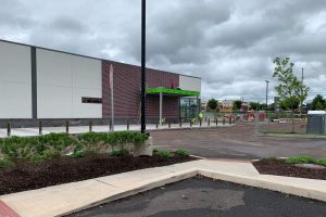 Why Businesses Spend More on Repairs Than Proper Structured Cabling Installation 1 New commercial retail building under construction with a green entrance canopy, workers in high-visibility gear, and freshly poured sidewalks under a cloudy sky.