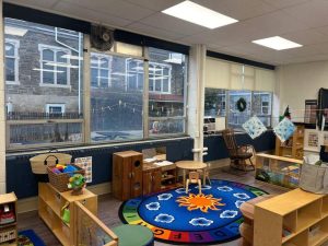 Structured Cabling in Philadelphia: Why Schools Invest? 3 Preschool classroom with a colorful alphabet rug featuring a sun design, wooden furniture and storage cubbies, a rocking chair, small tables, and large windows along one wall.