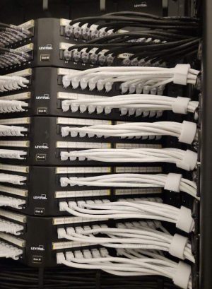 Why Structured Cabling Companies Prevent Service Tickets? 3 Stacked Leviton Cat 6 patch panels with labeled ports and neatly bundled white and black Ethernet patch cables secured with Velcro straps done by Bridge Cable, the top of structured cabling companies