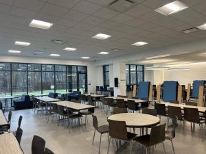 Structured Cabling in Philadelphia: Why Schools Invest? 4 Empty school cafeteria with round and rectangular tables, wooden chairs, blue folding lunch tables stacked upright in the background, and large windows overlooking a wooded area.