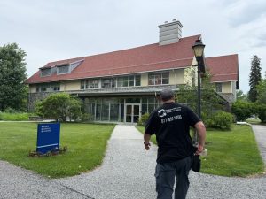 Structured Cabling in Philadelphia: Why Schools Invest? 6 A Bridgecable.com technician walks up a path toward the Rorer Science Building, a two-story stone building with a red shingled roof, large windows, and a glass entryway, with a blue building sign in the foreground.