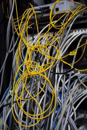 Why Structured Cabling Companies Prevent Service Tickets? 2 Messy bundle of yellow and gray Cat6 network cables tangled around a MikroTik switch and patch panels in a server rack done by other structured cabling companies