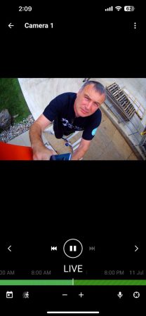 CCTV Contractor: CCTV vs AI Video Analytics in 2026 3 Live security camera app view showing a technician on a ladder outdoors, looking up toward the camera while holding a phone, with a "Camera 1" label and live playback controls visible.