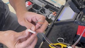 What Factors Affect a Structured Cabling Budget? 2 Technician preparing color-coded fiber optic strands for fusion splicing beside a splicing machine.