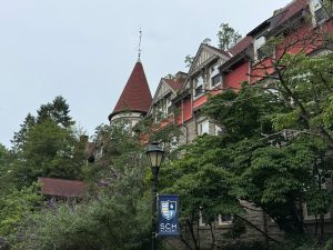 Summer Network Upgrades: WAPs & School Security 1 Historic stone-and-timber SCH Academy building with a red turret roof, framed by trees, with an SCH Academy banner on a lamppost in the foreground.