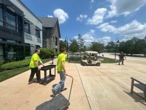 How Weather Extremes Affect Your Security Surveillance 2 Technicians in safety shirts pushing equipment carts outside a commercial building on a sunny day.