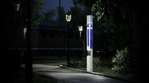 What Are Blue Light Emergency Towers at Hospitals? 1 White emergency call tower with a lit blue beacon and "EMERGENCY" signage on a paved path at night, illuminated by nearby streetlights among trees.