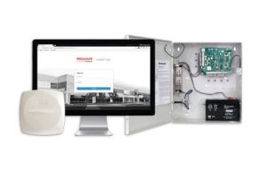 What Is Hybrid Access Control and How Does It Work? 1 Honeywell NetAXS-123 access control kit showing an open wall-mounted control panel with circuit board, power supply, and backup battery, a wireless door reader, and a monitor displaying the NetAXS-123 web-based sign-in portal.