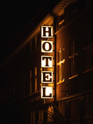 What's New in Hotel Keyless Entry Technology? 3 Vertical illuminated "HOTEL" sign glowing amber against a dark brick building facade at night, with lit windows visible on either side.