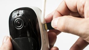 Cloud vs. Local: Which Security Camera Storage Wins? 2 Close-up of a hand inserting a black microSD memory card into the side slot of a white and black wireless security camera.
