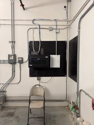 What Is Hybrid Access Control and How Does It Work? 3 Wall-mounted low-voltage equipment closet showing a Verkada access control panel, EarthLink modem, network switch in a Tripp-Lite rack, blue Ethernet patch cables in conduit, a ceiling-mounted security camera, and a grounding bus bar.